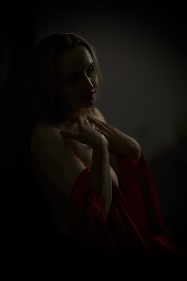 Low-key portrait with red satin drape, hand on shoulder